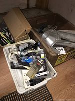 Photo showing mixed electrical parts including switches, outlet faceplates, and aluminum posts in a box and bin.