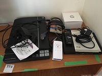 Shows the Epson V370 scanner with its power cable and installation CD, along with the Sony Blu-ray player on the right side with miscellaneous cables and a white power bar in front.