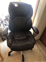 Full front view of the black executive chair showing padded back, head rest and cushioned seat on carpeted floor.