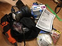 Lot overview with Black & Decker oscillating multi tool, orbital sander, sanding discs, dust mask, and user manual arranged on floor.