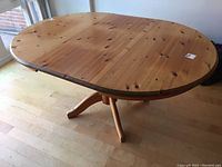 Oval knotty pine table top with visible wood grain and knots, showing scratches and wear marks. Table has an extension leaf.