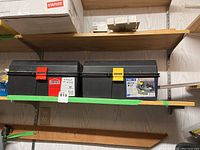 Two black plastic toolboxes on a wooden shelf with colored latches (red and yellow) labeled for angle grinder and Rotozip.