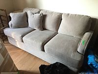 Front and left side view of the gray upholstered couch with cushions, showing wear and fabric texture.