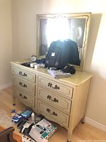 Full view of six drawer dresser with attached mirror and visible items on top and floor around it.