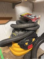 Photo showing yellow and black Shop-Vac with coiled hose and wrapped power cord.