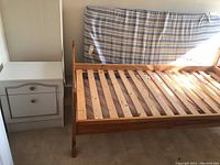 Pine single bed frame alongside the white bedside table, showing the bed slats and mattress leaning against the wall.