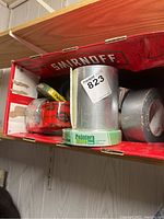 Photo showing various rolls of tape inside a Smirnoff box, including silver duct tape, green Painter's Mate tape, and red tuck tape.