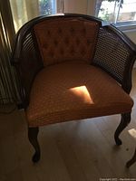 Full view of the burnt orange upholstered tub chair with caned sides and cabriole legs.