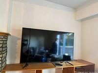 Front view of Samsung flat screen TV on stand with remote on cabinet. Black bezel with reflection visible.