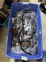 Blue plastic bin filled with numerous new Guess belts, mostly black and brown, in plastic packaging.