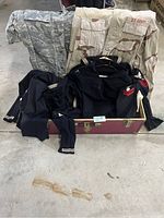 Photo showing two army camouflage uniforms (a desert pattern US Army jacket size large and an Air Force shirt) behind two folded navy dress uniforms with rank insignias, all placed atop a large maroon chest/trunk on a concrete floor.
