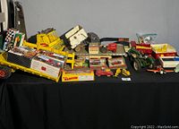Overview of the lot showing multiple vintage toy vehicles and boxed cars on a black cloth surface.