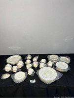 Full view of bone china set for 8 people laid out on black cloth, all items wrapped in original plastic.