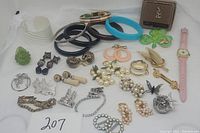 Full lot of vintage costume jewelry items arranged on white background showing earrings, bracelets, pins, rings, and watch.