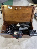 Open wooden chest showing electric train set including black locomotive, tracks, bridge, and controllers