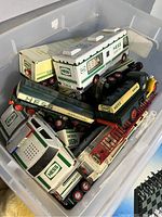Box with multiple vintage Hess toy trucks including camper, tanker, fire truck, police car, all with Hess branding.