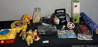 Full lot shot showing assortment of children's toys, PS2 console with controllers, portable radio, angel figurine, toy car, comic, and various accessories.
