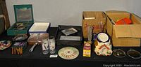 Wide shot of various kitchen items spread on a black table, including glassware, metal trays, containers, and decorative tins.