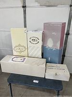 Five boxed porcelain collectible dolls from noted brands grouped together on a small table, showing original packaging.