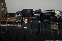 Photo showing a variety of vintage radios, cameras, binoculars and other electronic equipment on a table