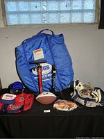Lot laid out on black surface near window with instant screen bag, football, small baseball, blue helmet, and red and blue duffel bag