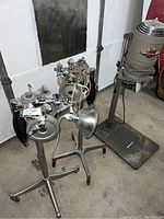 Wide shot showing several vintage medical equipment stands with attached photo and oxygen exposure meters, lamps, and a large floor-scale in warehouse.