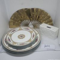 Set of plates stacked showing delicate floral and gold pattern with brass dragon fans and ceramic vase in background