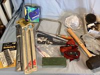 Photo showing the hacksaw, mallet, wire bending jig, sharpening stone, and respirators laid out on a bed surface.