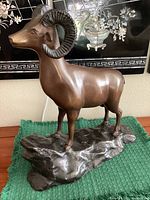 Full profile view of bronze ram statue standing on base.