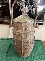 Front full view of carved bronze pot showing body motifs, lid and bail handle