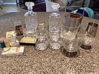 Wide angle photo showing two cut crystal decanters, various bowls, ice buckets, and bar accessories on kitchen countertop