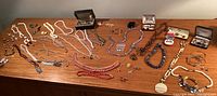 Overview of multiple necklaces, bracelets, brooches and other items laid out on wooden surface
