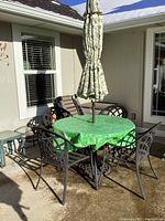 Full view of black metal patio set on concrete patio, table with green tablecloth and umbrella, four chairs