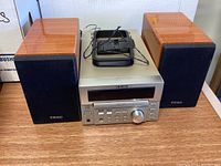 TEAC silver CD player and radio unit with two wood laminate speakers and a black accessory on top