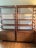 Front view of two teak open bookshelves each with three shelves and two-door cabinet base