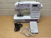 Front view of Brother SQ9050 sewing machine with power cord and foot pedal displayed in front.