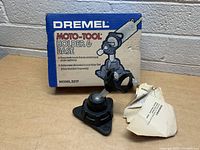Dremel Moto-Tool Holder & Base Model 2217 with original box and instructions on a table against a brick wall background.