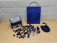 Full view of the lot showing all dice, wooden box, hanging sign, and mesh pouch on a wooden table against a gray brick wall.