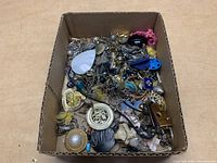 Full view of jewelry lot in cardboard box showing mixed jewelry pieces piled together