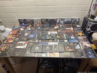 Photo showing a large assortment of unopened packaged CDs displayed on a table spread out, showing variety of album covers and genres.