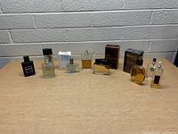 Overview of the lot of 8 assorted men's colognes presented on a wooden surface against a gray cinder block wall.
