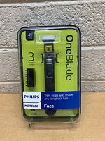 Front clear plastic packaging showing Philips OneBlade face trimmer with 3 stubble comb attachments, green and black casing.