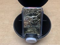 Close-up of the gold plated Pikachu trading card inside the open black Pokeball case.