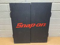 Closed black wooden cabinet with Snap On logo on front.