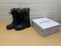 Pair of black winter boots with faux fur trim and laces next to a Top Moda shoe box.