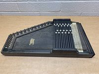 Side view of vintage autoharp showing full length with chord bars, multiple metal strings, and tuning pins.