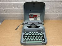Open hinged metal case revealing Hermes 3000 typewriter inside