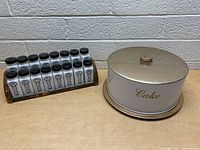 Photo showing the full lot: 18 milk glass spice jars in wooden spice rack, next to metal cake tray with lid