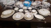 Full layout of 12 piece floral formal place setting including plates, bowls, cups, saucers, serving dishes arranged on table before packing.