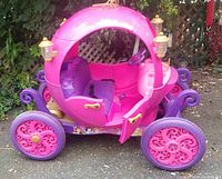 Side view of the pink and purple Cinderella carriage with a gold crown on top, showing one door open and intricate wheel design.